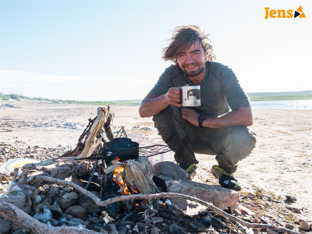 Eventyrar Jens Kvernmo sitter på huk foran et bål med en kopp i hånden. Han smiler og ser ut til å være i sitt ess. - Klikk for stort bilde